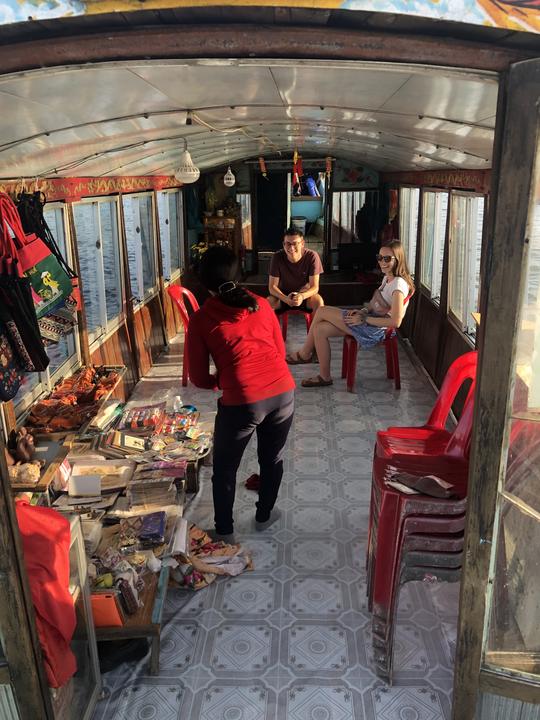 Die Besitzerin des Drachenboots zeigt Mikayla und Paul ihre Souvenirwaren